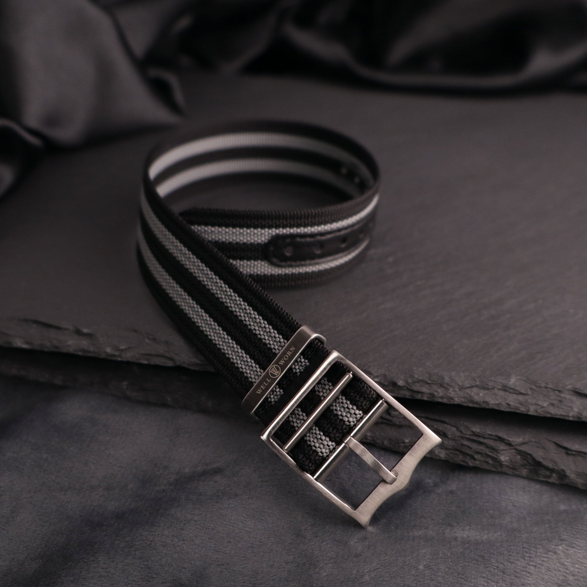 Black and gray striped belt with a silver buckle on a dark fabric background
